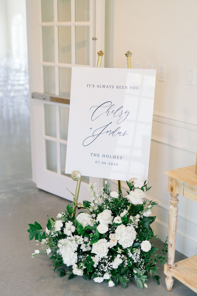 White acrylic wedding welcome sign on an easel with white and green florals