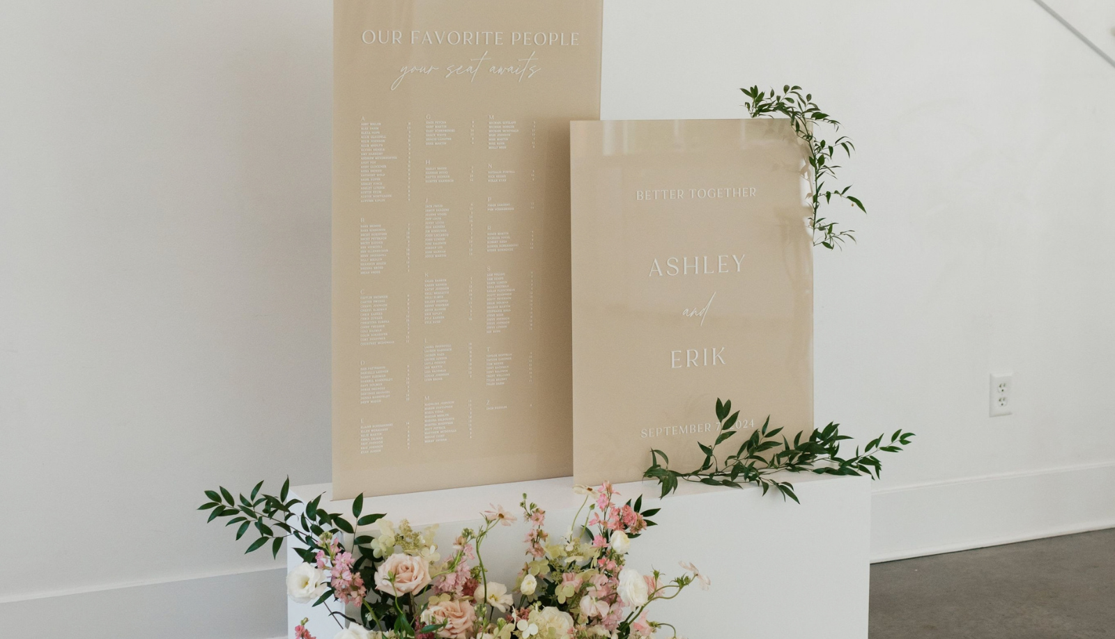 Two elegant custom acrylic wedding signs displayed together on white pedestals with fresh floral arrangements — a large seating chart titled 'Our Favorite People' and a welcome sign for Ashley and Erik